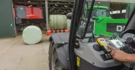 Włączanie stojącego przed oborą modelu owijarki RW 1110 za pomocą pilota zdalnego sterowania. W tle robot podający.