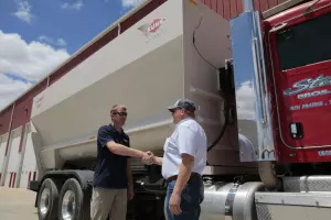 A KUHN Dealer shaking hands with a customer while standing in front of a KUHN Knight ProFeed delivery box.