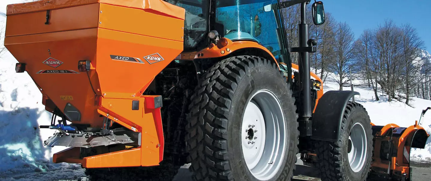 Rozsiewacz RAUCH AXEO do soli, piasku, żwiru i nawozu salt, podczas pracy na ośnieżonej górskiej drodze (ujęcie z narciarzem)