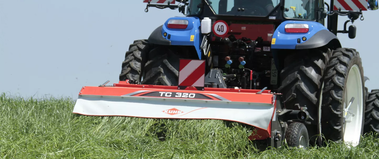 Zgniatacz pokosu TC 320 podczas pracy w wysokiej trawie z traktorem na podwójnych kołach.