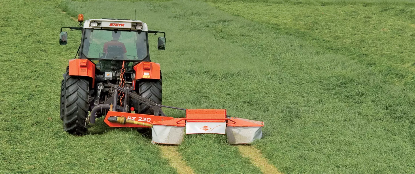 Kosiarka bębnowa PZ 220 ze zgniataczem pokosu kosząca trawę na płaskim polu.