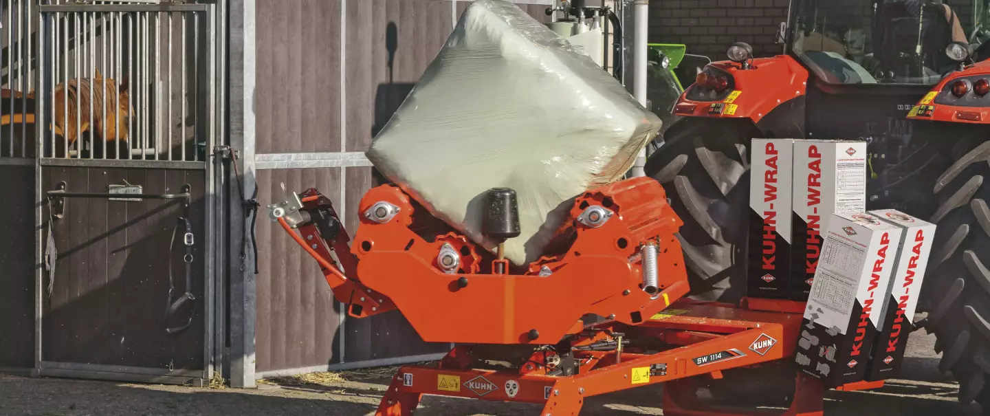 Pracująca w miejscu owijarka bel prostopadłościennych SW 1114 stojąca przed stajnią